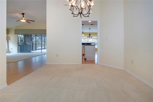 spare room featuring vaulted ceiling, carpet flooring, and ceiling fan with notable chandelier