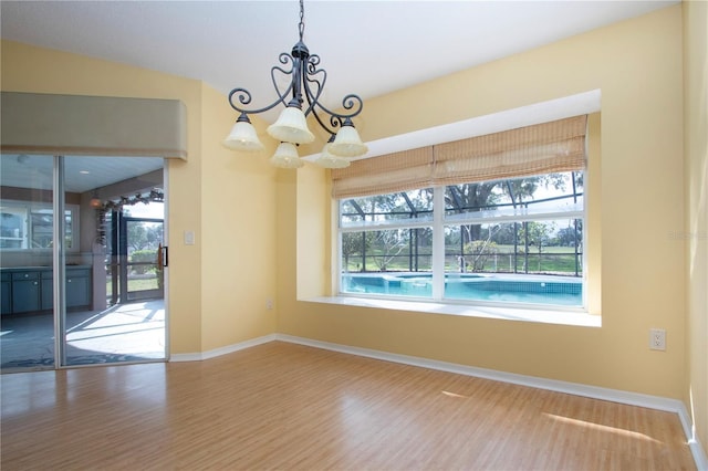 spare room featuring an inviting chandelier, wood-type flooring, and plenty of natural light