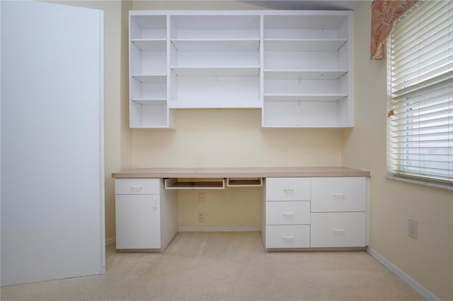 unfurnished office featuring built in desk and light colored carpet