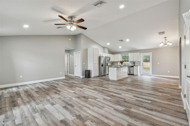 unfurnished living room featuring ceiling fan with notable chandelier, light wood-type flooring, and vaulted ceiling