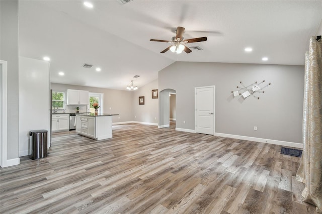 unfurnished living room featuring ceiling fan with notable chandelier, light wood-type flooring, and vaulted ceiling