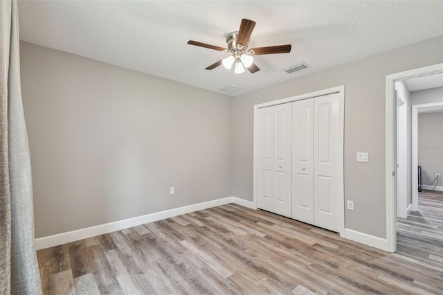 unfurnished bedroom with a textured ceiling, a closet, light hardwood / wood-style flooring, and ceiling fan