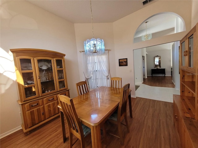 dining space with wood-type flooring, an inviting chandelier, and a high ceiling