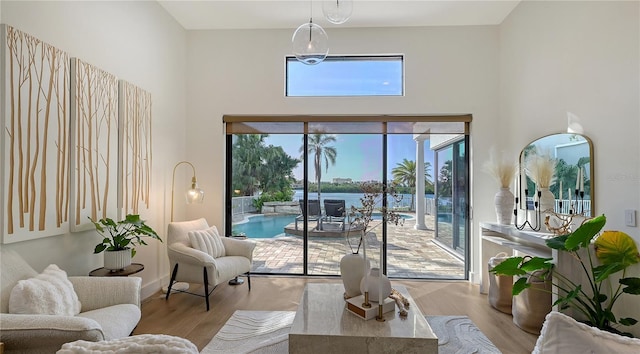 living room with a towering ceiling, a water view, and light hardwood / wood-style floors