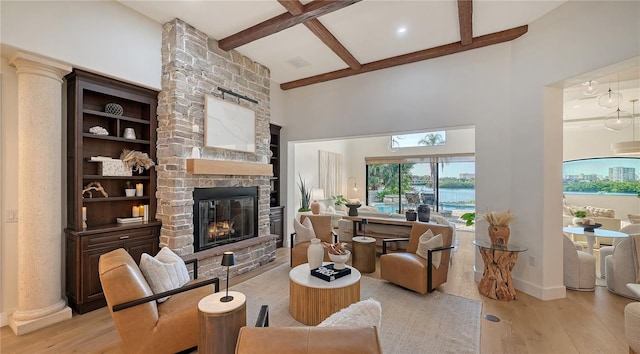 living room with coffered ceiling, a water view, a stone fireplace, light wood-type flooring, and beam ceiling