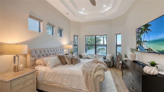 bedroom with a raised ceiling, a towering ceiling, light hardwood / wood-style flooring, and crown molding