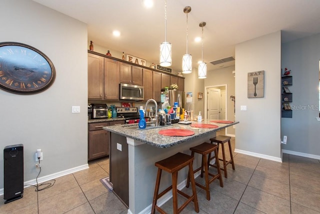 kitchen featuring a breakfast bar, stainless steel appliances, sink, pendant lighting, and an island with sink