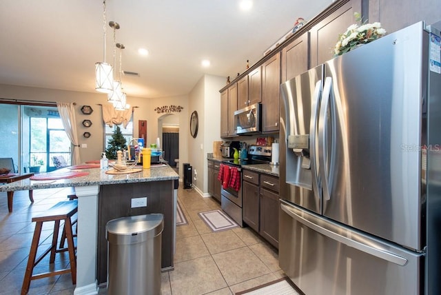 kitchen with a kitchen breakfast bar, a center island, light stone countertops, and appliances with stainless steel finishes