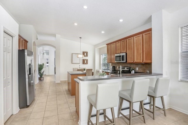 kitchen with kitchen peninsula, light tile patterned floors, stainless steel appliances, and decorative light fixtures