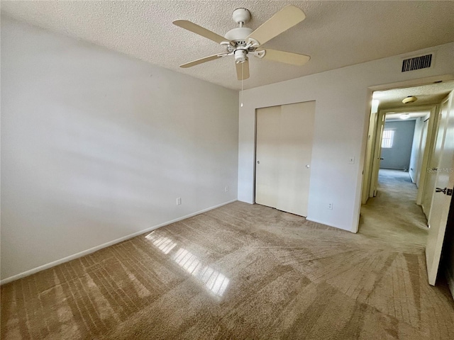 unfurnished bedroom with ceiling fan, a closet, light carpet, and a textured ceiling