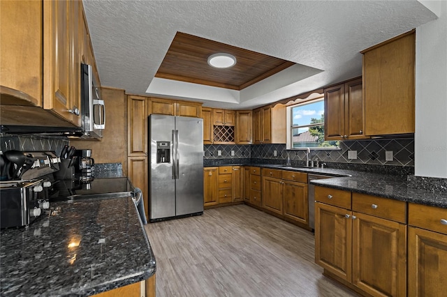 kitchen with stainless steel appliances, light hardwood / wood-style floors, sink, decorative backsplash, and a raised ceiling