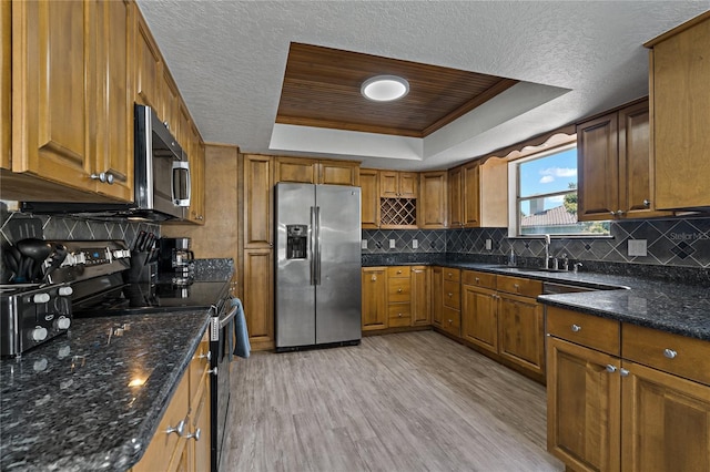 kitchen with light hardwood / wood-style floors, stainless steel appliances, a raised ceiling, backsplash, and sink