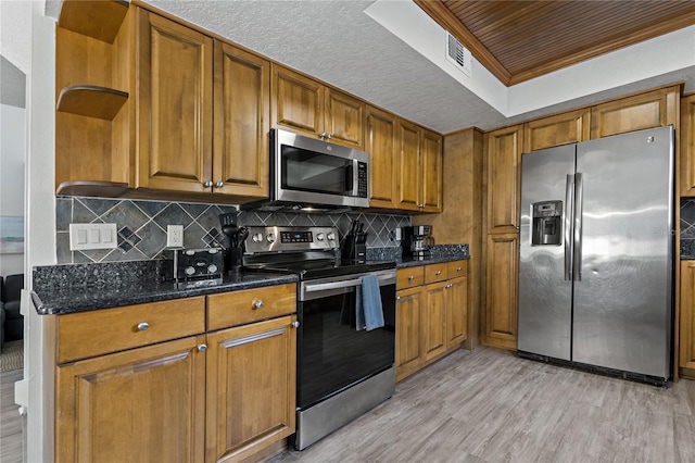 kitchen featuring stainless steel appliances, dark stone counters, light hardwood / wood-style floors, decorative backsplash, and crown molding