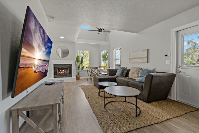 living room featuring ceiling fan, wood-type flooring, vaulted ceiling, and a textured ceiling