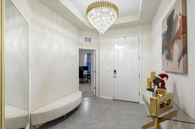 foyer entrance featuring a chandelier, light tile patterned floors, and a tray ceiling