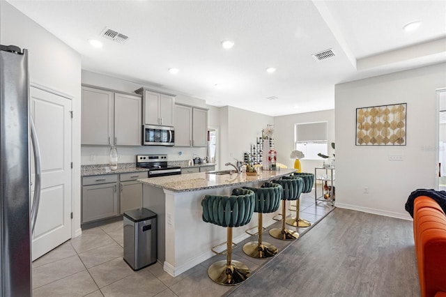 kitchen featuring sink, stainless steel appliances, a kitchen breakfast bar, gray cabinets, and a center island with sink