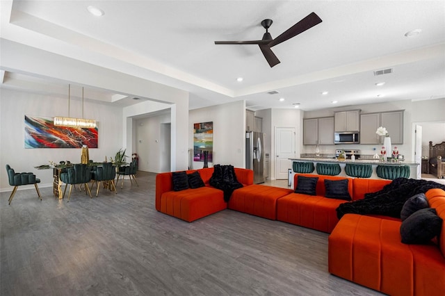 living room with a raised ceiling, dark hardwood / wood-style flooring, and ceiling fan with notable chandelier