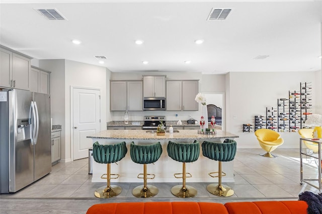 kitchen with a center island with sink, a kitchen breakfast bar, gray cabinets, and stainless steel appliances