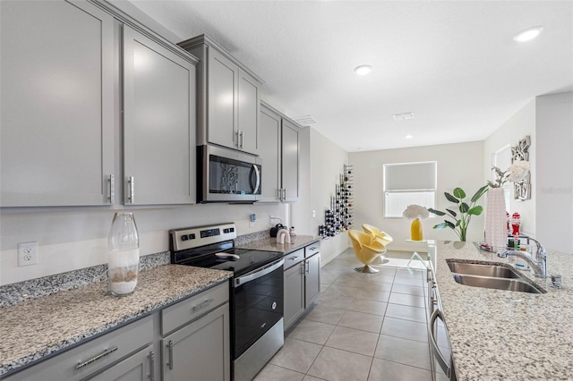 kitchen featuring appliances with stainless steel finishes, light stone counters, sink, light tile patterned floors, and gray cabinets