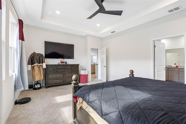 bedroom with ceiling fan, light colored carpet, connected bathroom, and a tray ceiling