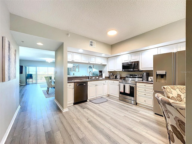 kitchen featuring sink, stainless steel appliances, light hardwood / wood-style flooring, a textured ceiling, and white cabinets