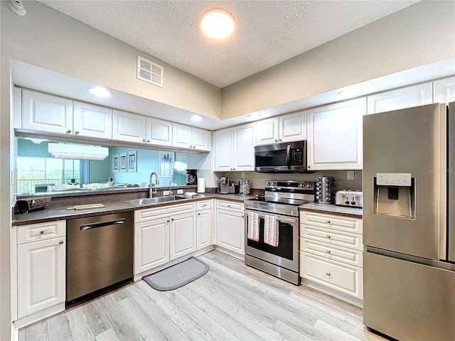 kitchen featuring appliances with stainless steel finishes, a textured ceiling, white cabinetry, and sink