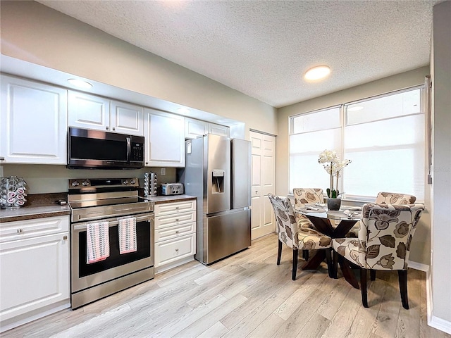 kitchen with appliances with stainless steel finishes, a textured ceiling, light hardwood / wood-style flooring, and white cabinetry