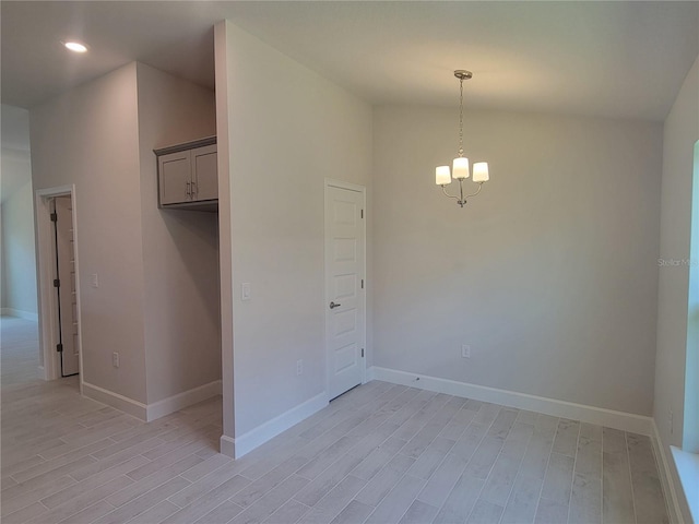 spare room with light wood-type flooring, a towering ceiling, and an inviting chandelier