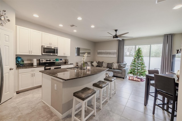 kitchen with white cabinetry, ceiling fan, stainless steel appliances, dark stone counters, and a breakfast bar area