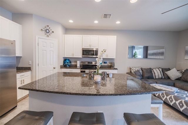 kitchen featuring dark stone counters, a breakfast bar area, a kitchen island, white cabinetry, and stainless steel appliances