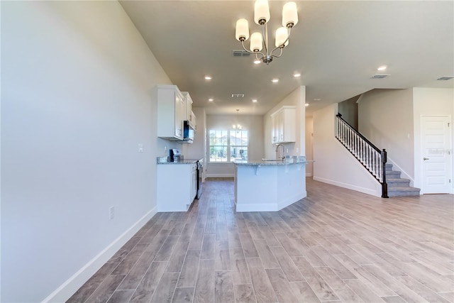 kitchen featuring light stone counters, a chandelier, light wood-type flooring, stainless steel electric stove, and white cabinets