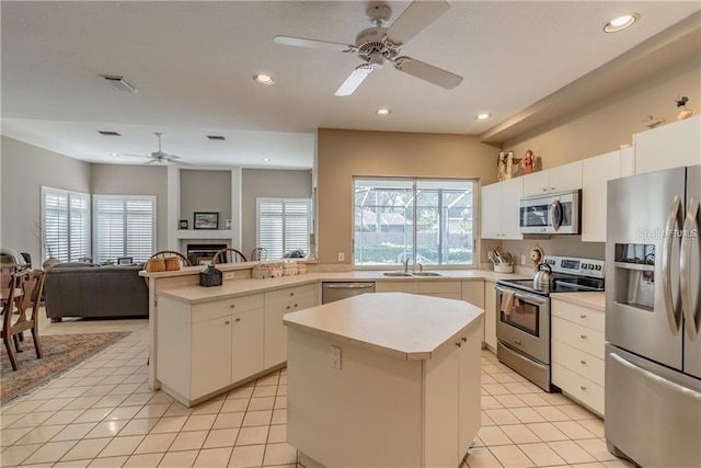 kitchen featuring appliances with stainless steel finishes, sink, light tile patterned floors, white cabinets, and a center island