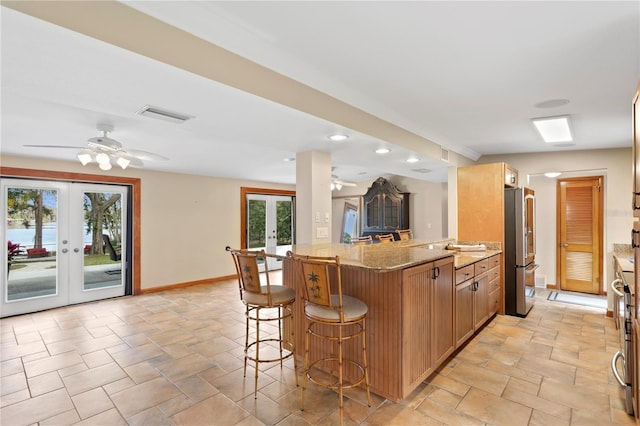 kitchen with a breakfast bar, plenty of natural light, kitchen peninsula, high end refrigerator, and french doors