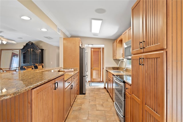 kitchen featuring ceiling fan, stainless steel appliances, sink, and dark stone counters