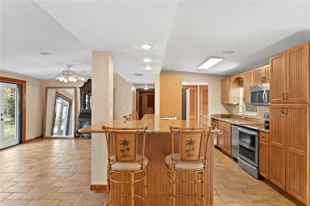 kitchen with a kitchen breakfast bar, a center island, ceiling fan, light stone counters, and stainless steel appliances