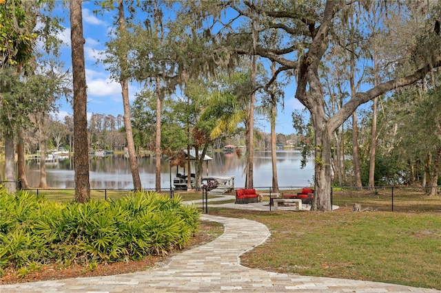 view of community featuring a lawn, a water view, and fence