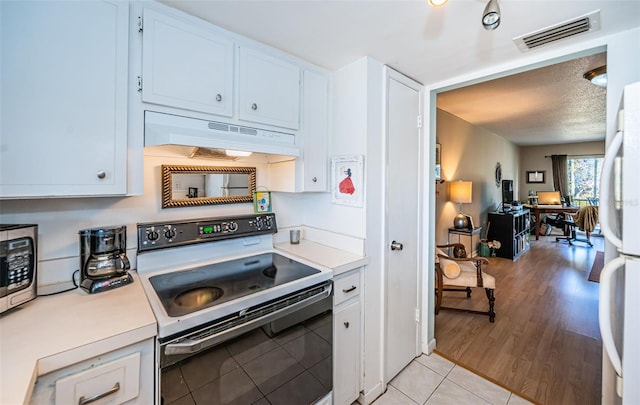 kitchen featuring light tile patterned floors, white fridge, white cabinetry, and range with electric stovetop