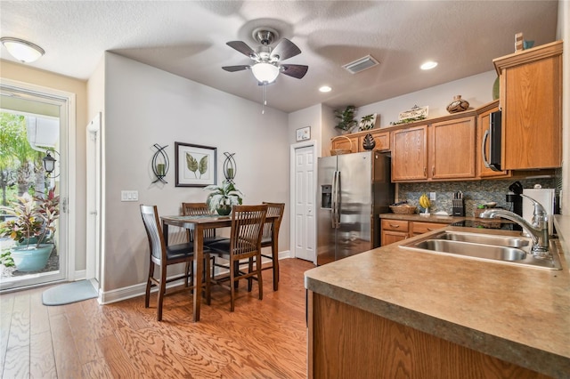 kitchen featuring backsplash, sink, ceiling fan, light wood-type flooring, and appliances with stainless steel finishes