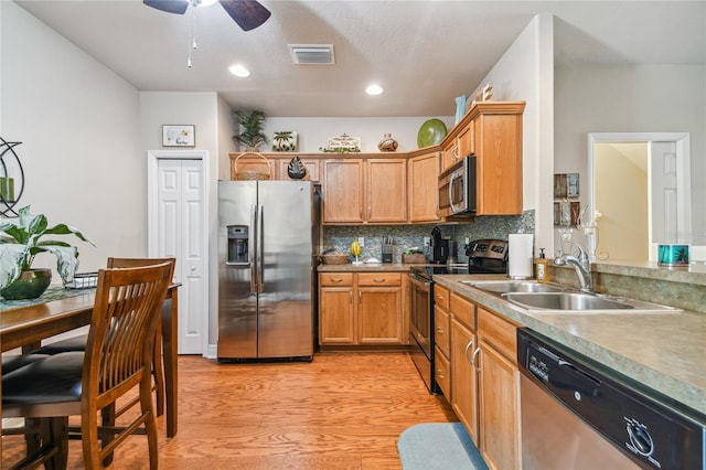 kitchen with appliances with stainless steel finishes, backsplash, ceiling fan, sink, and light hardwood / wood-style flooring