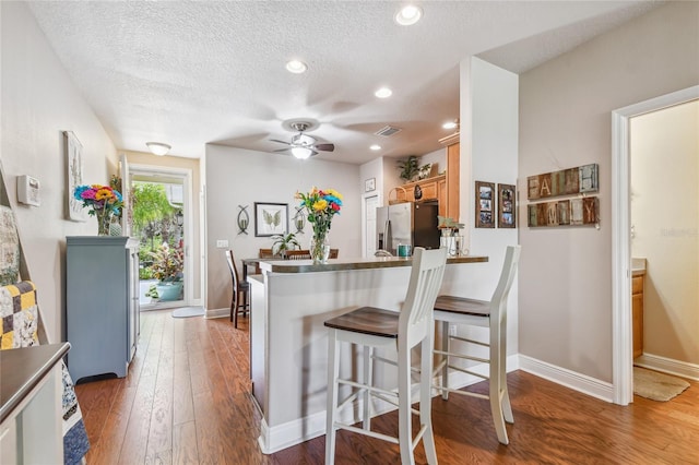 kitchen featuring kitchen peninsula, stainless steel refrigerator with ice dispenser, dark hardwood / wood-style flooring, a textured ceiling, and ceiling fan