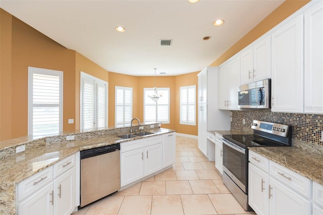 kitchen with appliances with stainless steel finishes, sink, light tile patterned floors, white cabinets, and hanging light fixtures