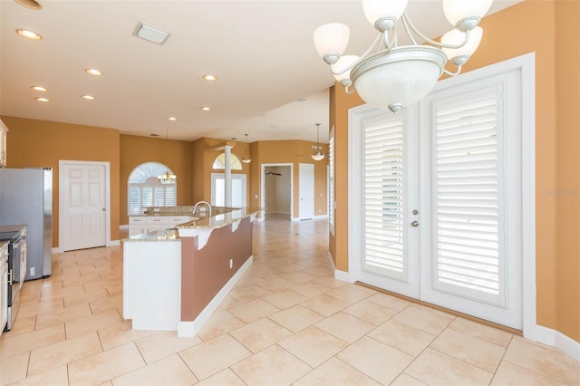 kitchen with appliances with stainless steel finishes, white cabinets, light stone counters, a chandelier, and hanging light fixtures