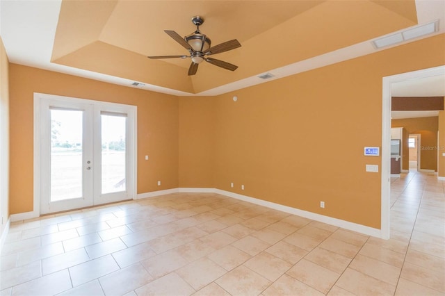 tiled spare room featuring a raised ceiling, ceiling fan, and french doors