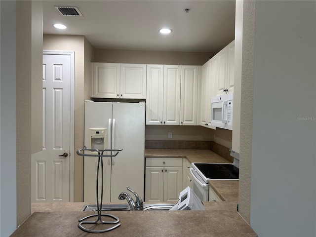 kitchen with sink, white appliances, white cabinetry, and kitchen peninsula