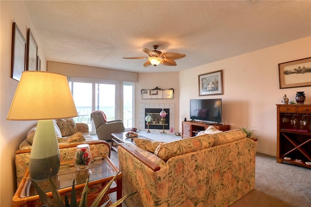 carpeted living room featuring ceiling fan, a textured ceiling, and a tiled fireplace