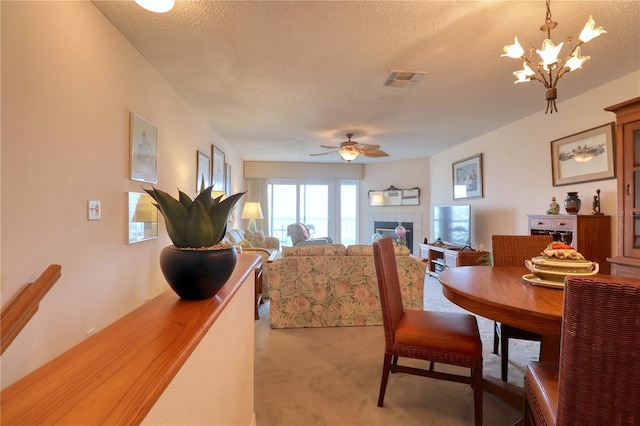 dining space with a textured ceiling, a tile fireplace, light colored carpet, and ceiling fan with notable chandelier