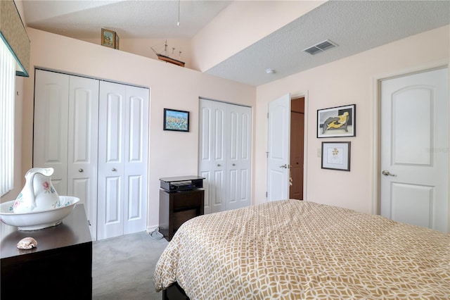 carpeted bedroom featuring a textured ceiling and two closets