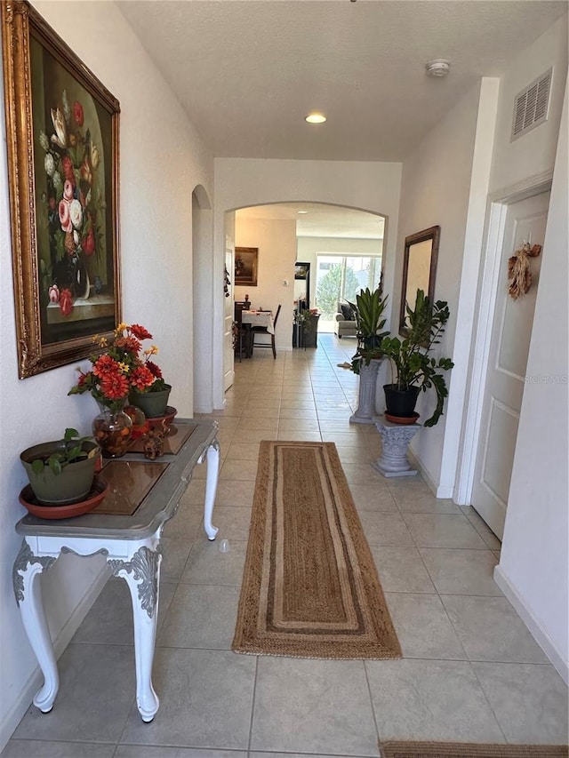 hall featuring arched walkways, recessed lighting, visible vents, light tile patterned flooring, and baseboards