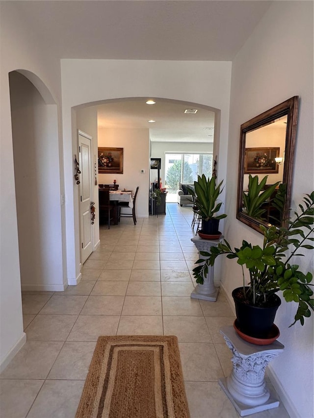 corridor with light tile patterned floors, baseboards, and arched walkways