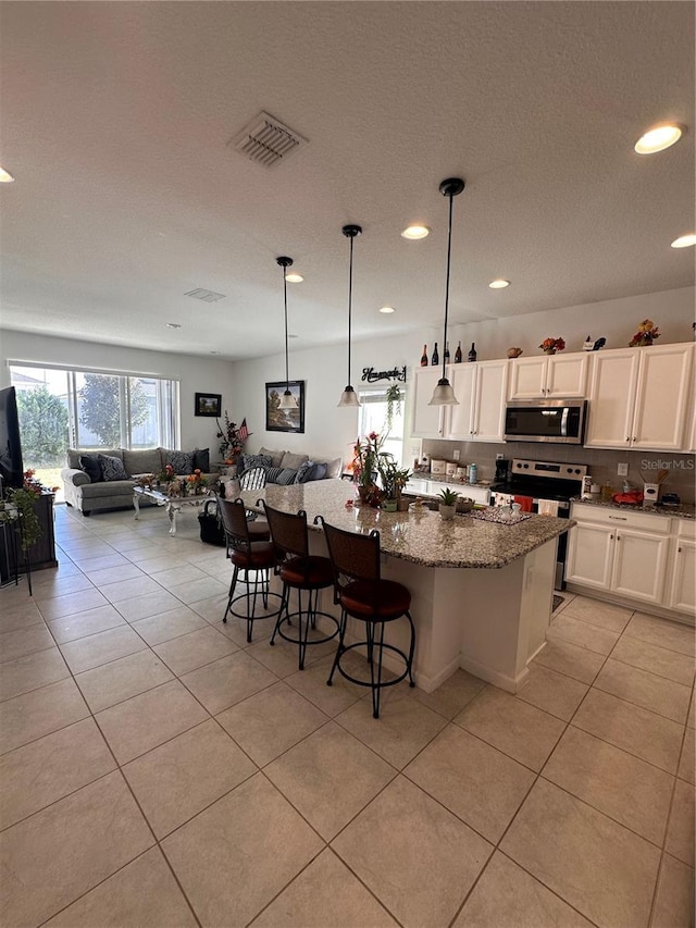 kitchen with visible vents, dark stone countertops, a kitchen island with sink, stainless steel appliances, and a kitchen bar